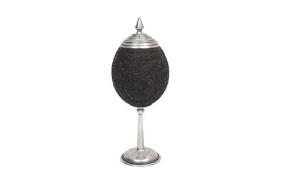 Lot 174 - AN ANGLO-INDIAN CARVED COCONUT SHELL WITH A HERALDIC SHIELD AND STAMPED SHEFFIELD 1878 SILVER MOUNTS
